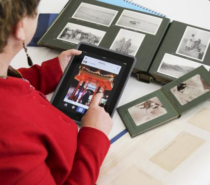 Woman holding tablet displaying a digital image with albums of photographs on a table