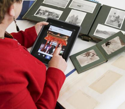 Woman holding tablet displaying a digital image with albums of photographs on a table