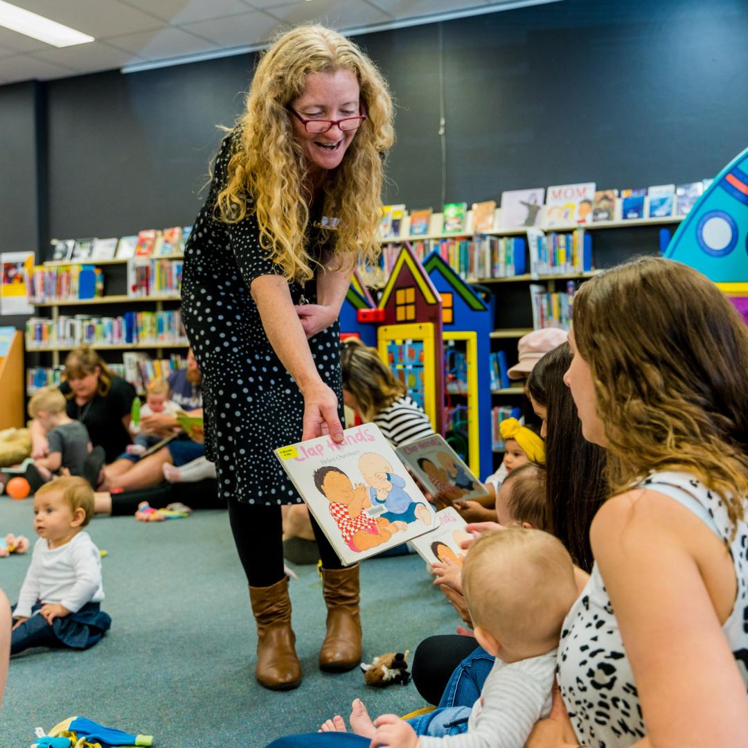 Person passing a book to a parent holding a baby in a library