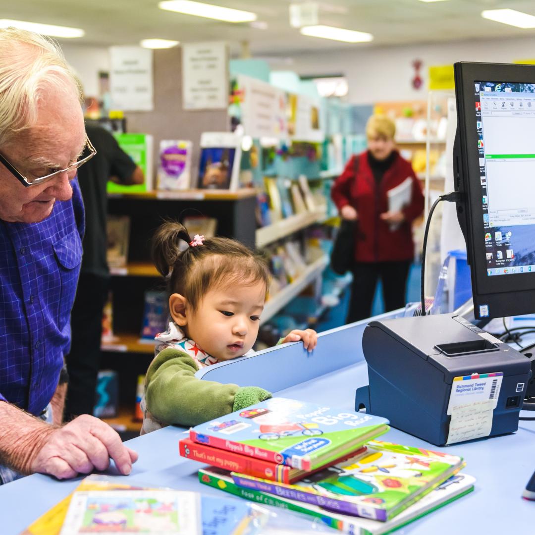 Older male and small child at a library service counter